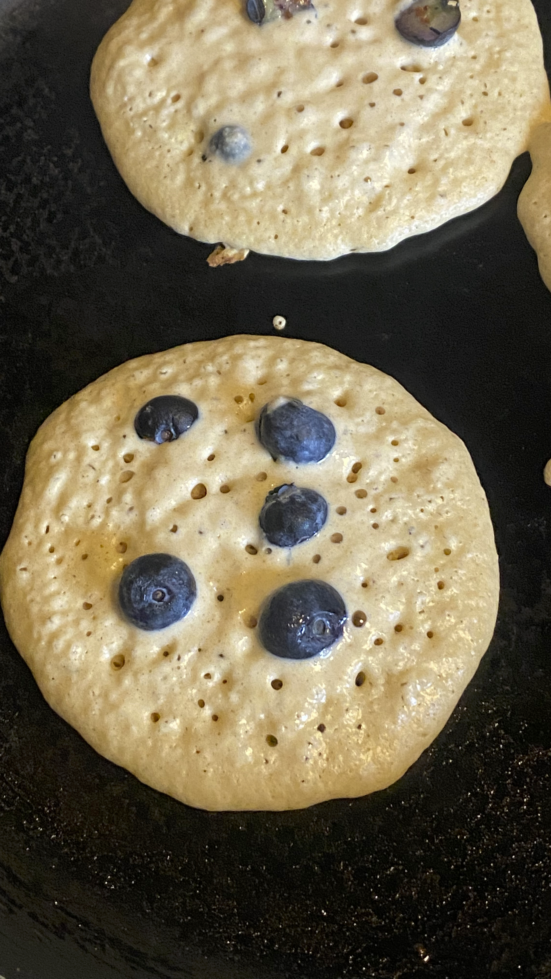 Pancake cooking in pan with blueberries on it